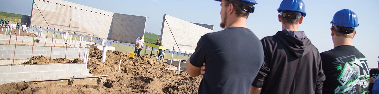 Students in blue hard hats facing away, looking at building site